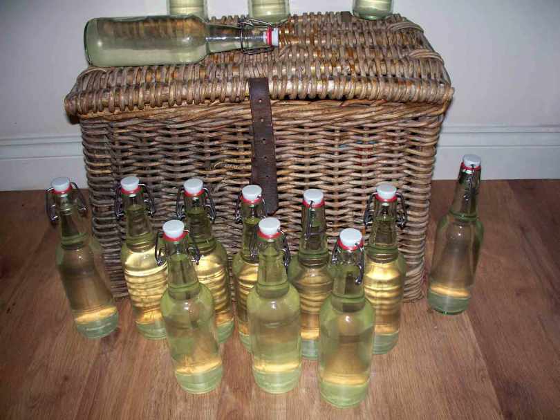Picture of bottles of Elderflower champagne next to a wicker fishing creel