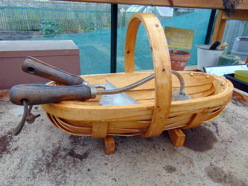 Picture of a small hand hoe and trowel in a wooden trug