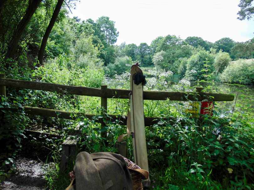 Picture of vintage fishing tackle with rod back leaning against an old wooden fence at the edge of a lake