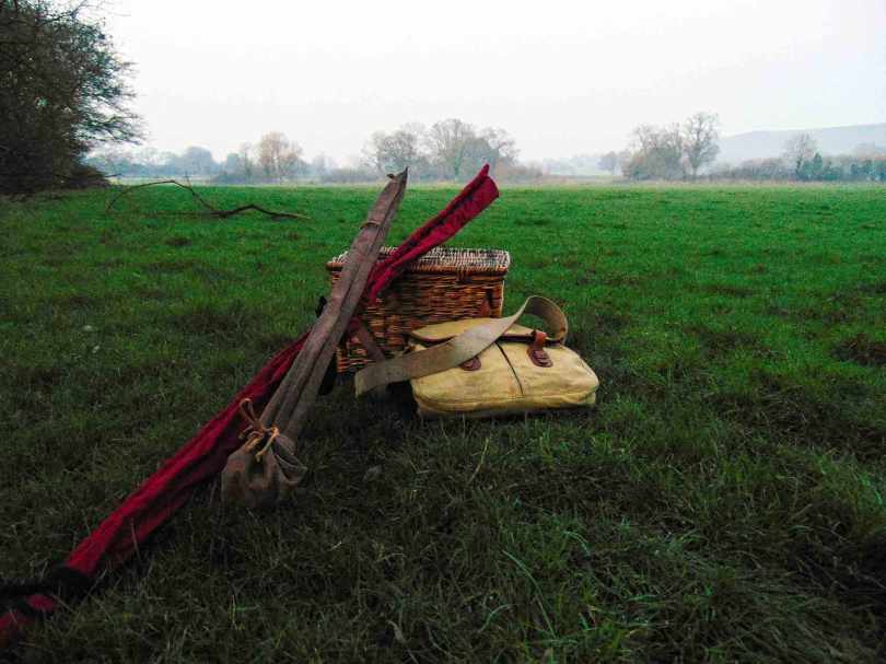 Picture of two fishing rods leaning against a wicker creel with a Brady bay lying along-side on the grass