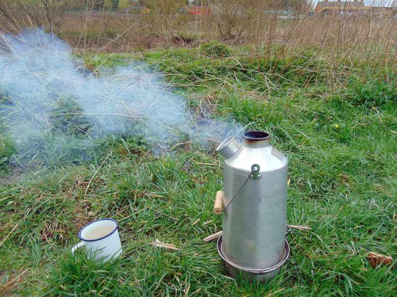 Picture of a boiling Kelly Kettle with mug ready for the hot water
