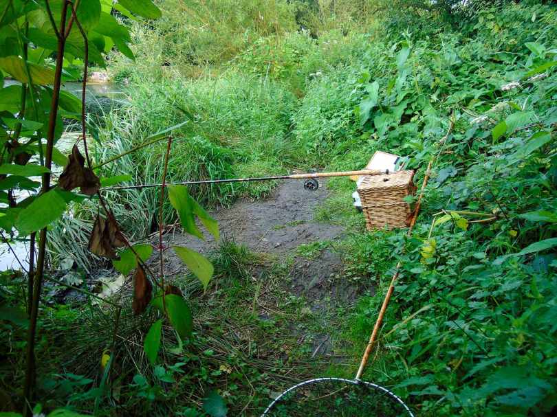 Picture of a vintage cane rod resting on a wicker creel with a vintage landing net on the ground